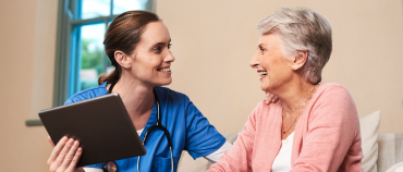 Healthcare pro in blue scrubs kneeling next to an elderly female patient
